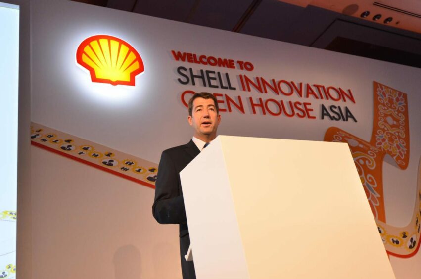 Man behind podium, with Shell logo over shoulder 