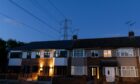 An electricity transmission tower near residential houses with lights on in Upminster, UK, on Monday, July 4, 2022.