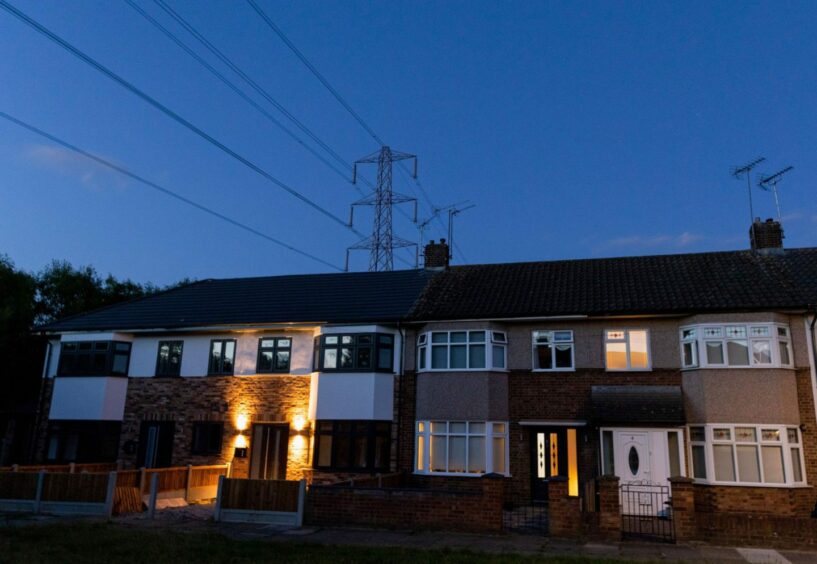 An electricity transmission tower near residential houses with lights on in Upminster, UK, on Monday, July 4, 2022.