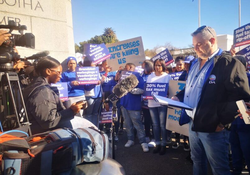 Man addresses camera crew, in front of crowd wearing blue