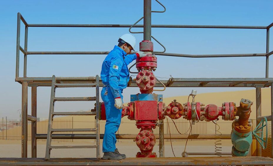 Man in blue next to red well equipment