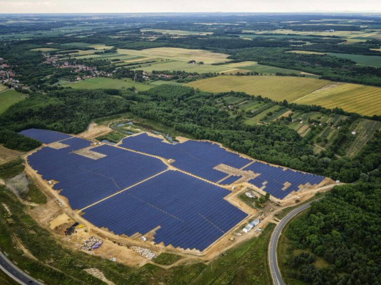 Aerial view of solar panels, surrounded by trees and green landscape