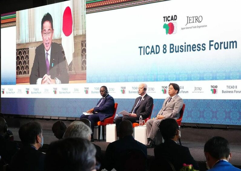 Man projected onto backdrop, with three sitting in front