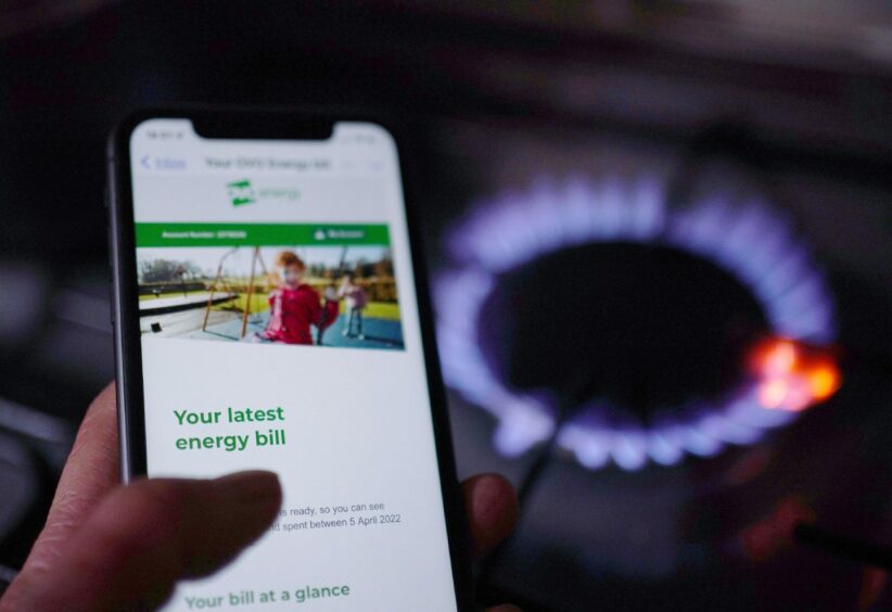 A general view of a household energy bill displayed on a mobile phone held next to a gas hob.