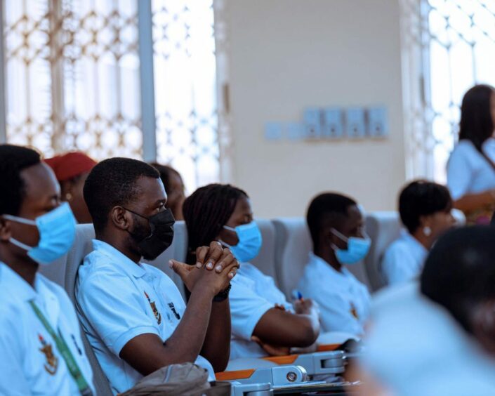 Students wearing blue shirts listen, with windows behind