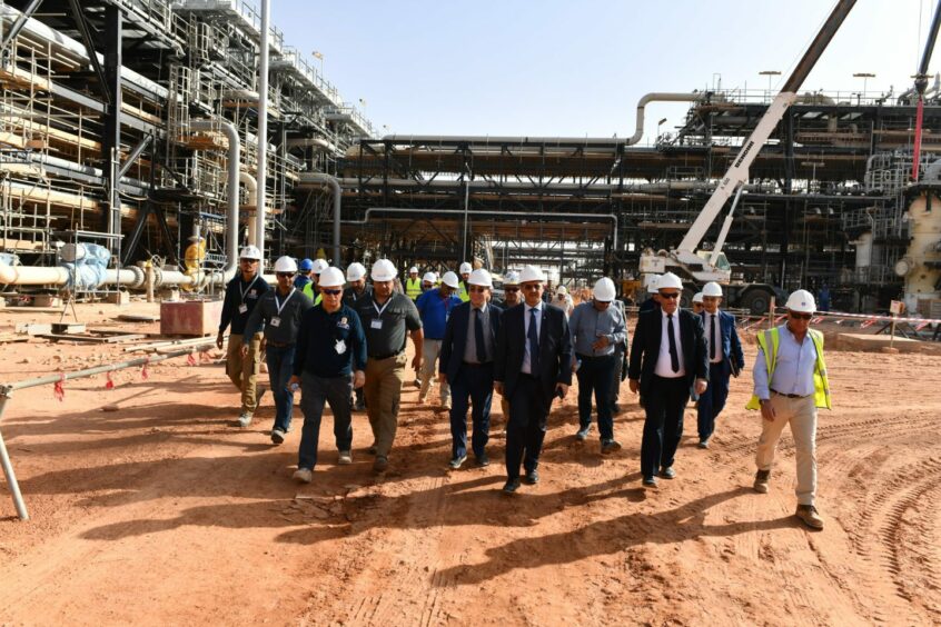 Men in hard hats walk over sand in industrial facility