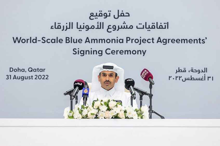 Man behind microphones in front of white backdrop with writing on it