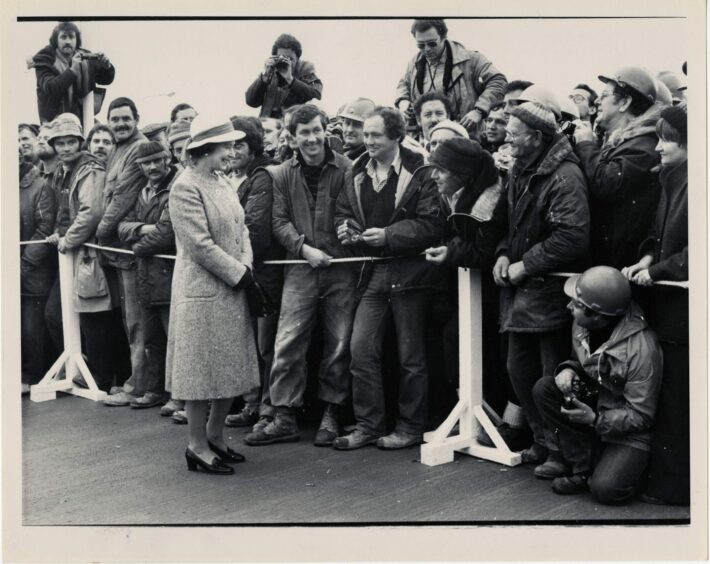 1981. Queen Elizabeth in a relaxed mood as she shares a joke with workers at the engineering workshop during the Royal visit to the Sullom Voe oil terminal.