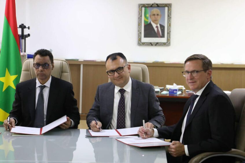 Three men sign documents at a table