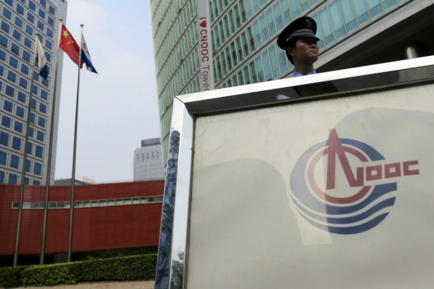 The Chinese national flag flies near a security guard outside the Cnooc Ltd. headquarters in Beijing, China, on Tuesday, July 24, 2012.  Photographer: Nelson Ching/Bloomberg