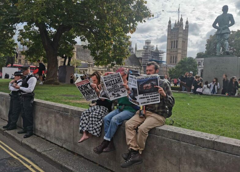 Demonstrators read mock up newspapers next to police