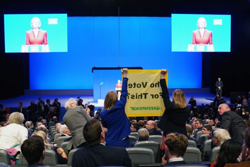 Demonstrators hold a banner as Prime Minister Liz Truss delivers her keynote speech at the Conservative Party annual conference at the International Convention Centre in Birmingham. Picture date: Wednesday October 5, 2022. PA Photo. See PA story POLITICS Tory. Photo credit should read: Jacob King/PA Wire