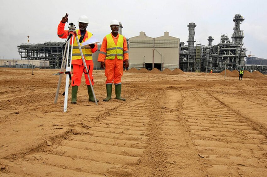 Two men in high vis vests stand on brown earth