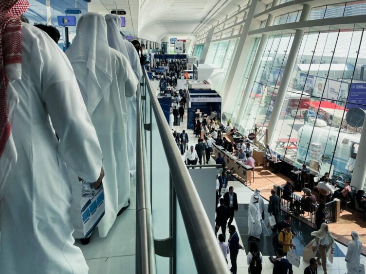 Men in white robes on balcony left, while on right people walk past