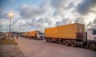 Lorry pulls orange trailers under cloudy sky
