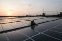 Worker amid solar panels on roof, as sun sets behind