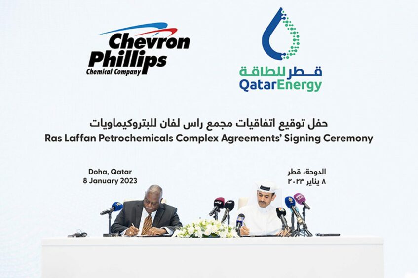 Two men sign documents in front of company logos