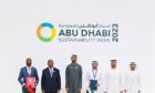 Men stand in front of white wall saying Abu Dhabi