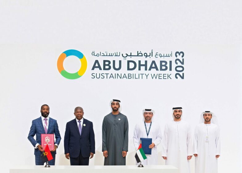 Men stand in front of white wall saying Abu Dhabi