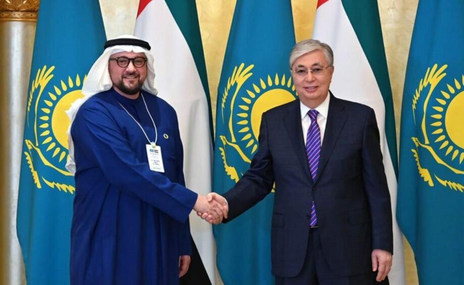 Two men shake hands in front of flags