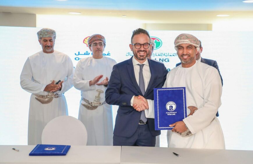 Men smiling shaking hands, one holds blue book