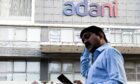 A man checks his mobile phone as he walks by the Adani logo on building in Mumbai. 2 Feb 2023