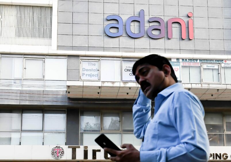 A man checks his mobile phone as he walks by the Adani logo on building in Mumbai. 2 Feb 2023
