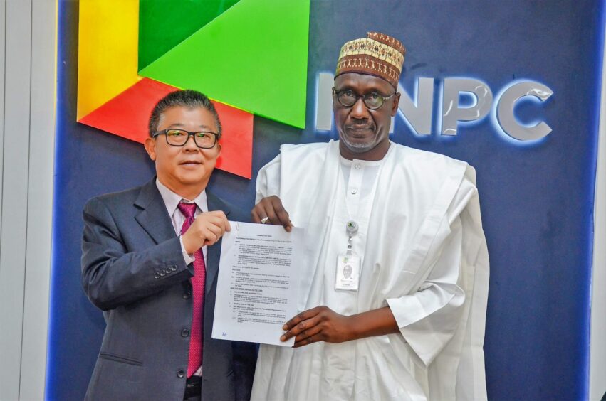 Two men hold document in front of NNPC backdrop