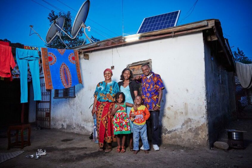 Family stand next to white wall, with solar panel above, washing line on left