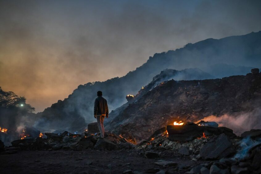 SONBHADRA, INDIA - NOVEMBER 22: A man stands near burning coal waste inside a coal mine on November 22, 2021 in Sonbhadra, Uttar Pradesh, India. India is rapidly transitioning to renewables, investing in widespread solar and wind installations, though it still remains reliant on coal for about 70% of its energy needs, media reports said. India's heavy reliance on coal was a key issue at the recent Cop26 conference. Many coal-producing regions within the country remain essential for the functioning of the economy, employing many thousands of laborers, though they have been criticized for what activists say is their contribution to air and groundwater pollution, as well as for the detrimental effects coal-related pollution is said to have on respiratory diseases. (Photo by Ritesh Shukla/Getty Images)