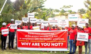 People in red hold up protests signs against EACOP