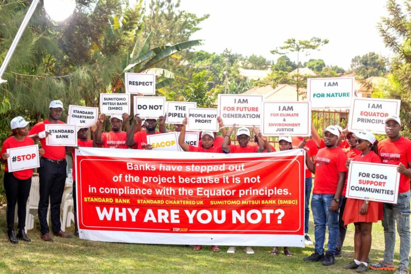 People in red hold up protests signs against EACOP 