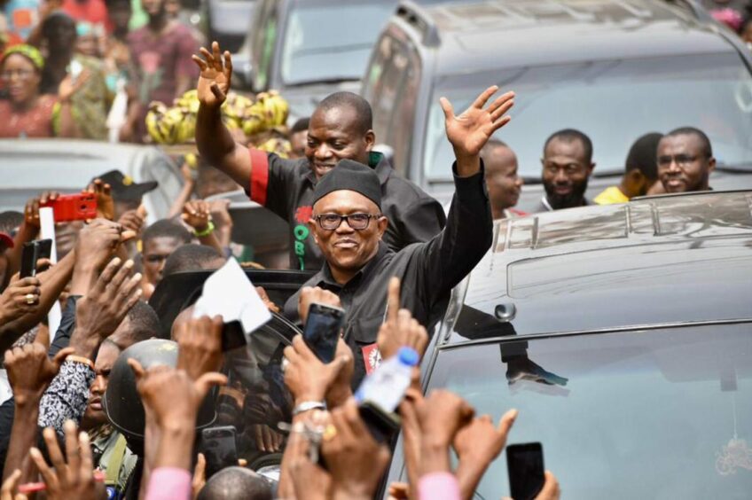 Man waves while getting out of a car, surrounded by people