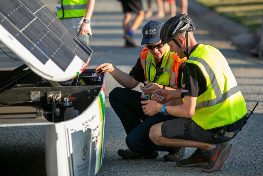 Two people in hi vis jackets look at a solar panel car