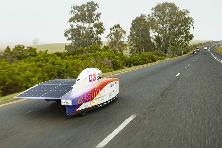 Solar car zooms down open road with trees on the side 