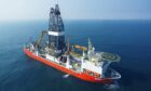 Drill ship with red hull in blue sea