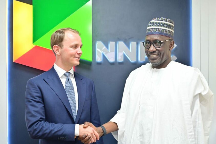 Two men shake hands in front of NNPC backdrop