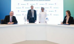 Baker Hughes and Adnoc officials sign a deal on new hydrogen technologies, behind white desk with logoed backdrop