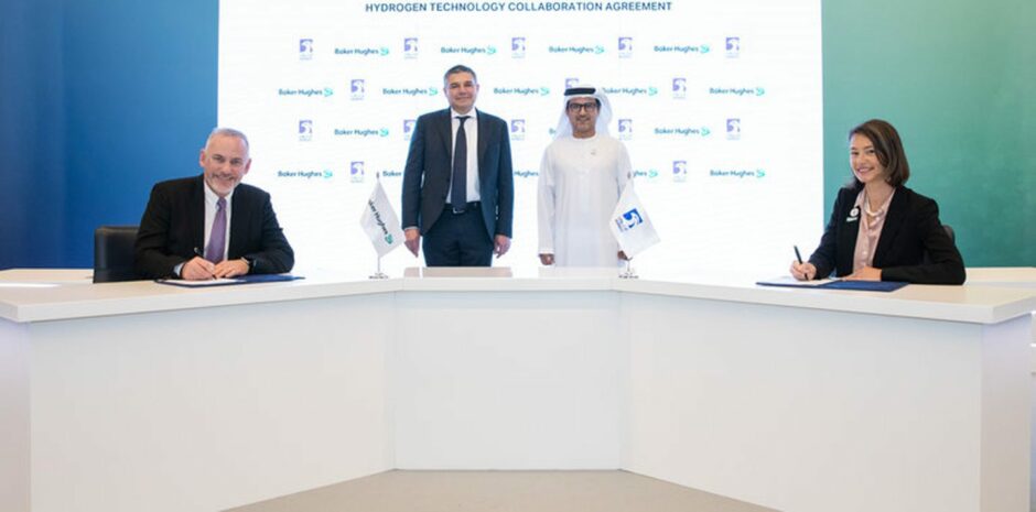 Baker Hughes and Adnoc officials sign a deal on new hydrogen technologies, behind white desk with logoed backdrop