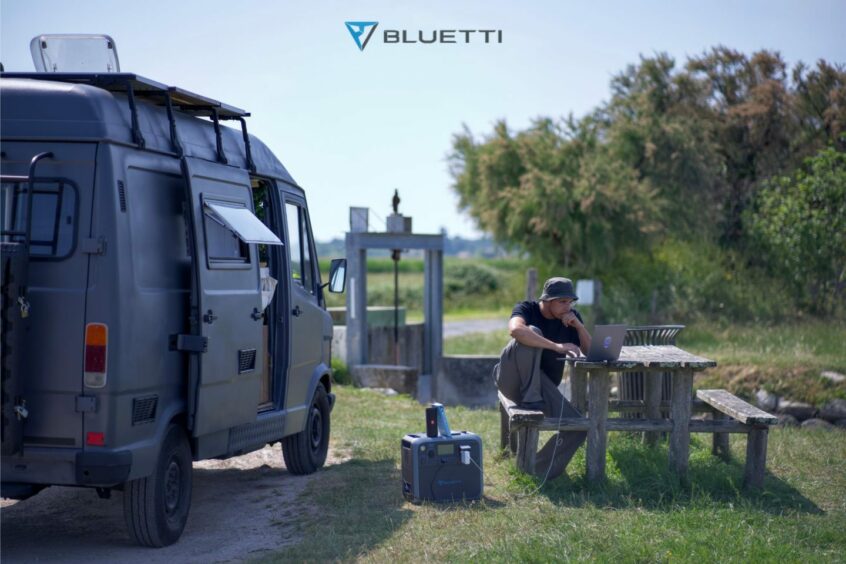 Man sat outside his camper van using the BLUETTI AC200P solar generator kit to power his laptop.