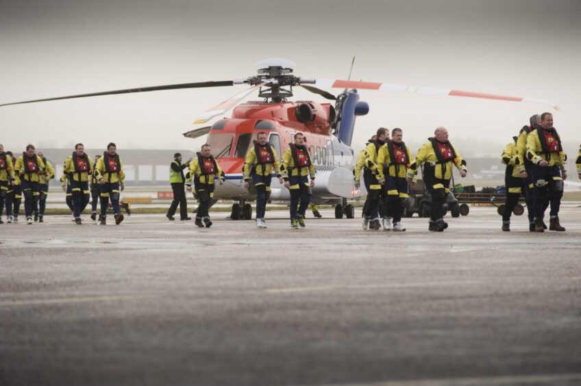 Offshore workers with a CHC Scotia helicopter at Aberdeen heliport.