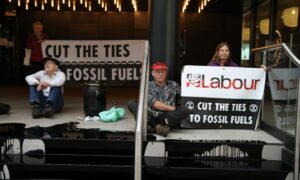Climate change protesters from the Extinction Rebellion group on steps covered in fake oil holding banners reading "Labour - Cut The Ties to Fossil Fuels"