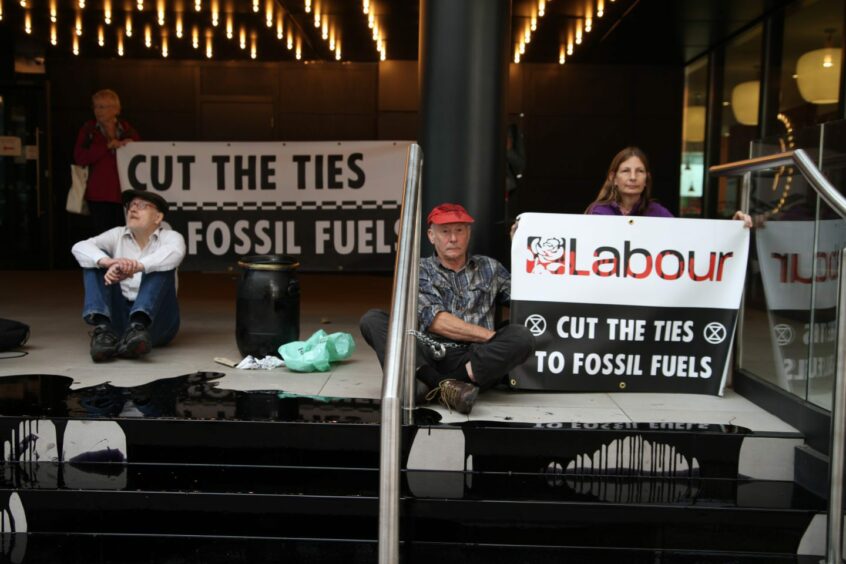 Climate change protesters from the Extinction Rebellion group on steps covered in fake oil holding banners reading "Labour - Cut The Ties to Fossil Fuels"