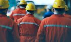 Energy workers in hard hats and overalls face away from camera.