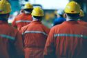 A group of men in overalls and hard hats walking away from camera.