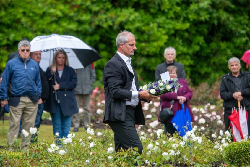 Steve Rae lays flowers at Piper Alpha memorial service as attendees watch from Aberdeen gardens.