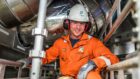 Bilfinger employee in orange boiler suit and white hard hat surrounded by metal pipes.