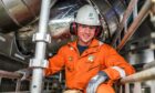 Bilfinger employee in orange boiler suit and white hard hat surrounded by metal pipes.