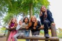 five girls smile while leaning over a barrier in a play area