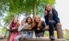 five girls smile while leaning over a barrier in a play area